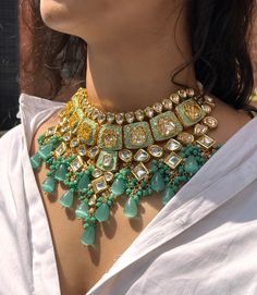 a close up of a woman's neck wearing a green and gold statement necklace