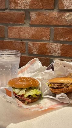 two hamburgers and a drink sitting on a table next to a brick wall in the background