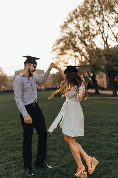 a man and woman are dancing in the grass at their graduation ceremony, with trees in the background