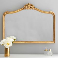 a gold framed mirror sitting on top of a white table next to a vase with flowers