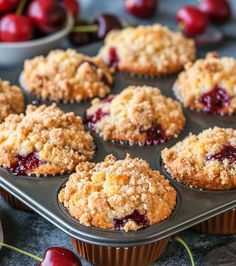 muffins with crumbs and cherries sitting on a baking tray next to bowls of cherries