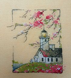 a cross stitch picture with a lighthouse and cherry blossom tree in the foreground, on a beige background