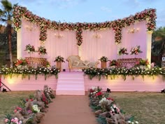 an outdoor wedding setup with flowers and greenery on the wall, pink carpeted stage