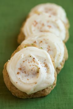 three cookies with icing sitting on top of a green cloth covered in white frosting