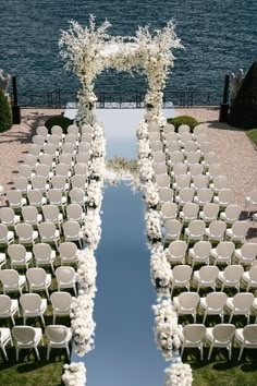 an outdoor ceremony setup with white flowers and chairs on the grass, overlooking the water