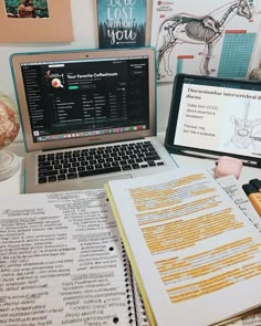 a laptop computer sitting on top of a desk next to an open book and notebook