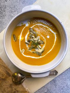 a white bowl filled with soup on top of a cutting board next to a spoon