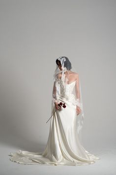 a woman in a white wedding dress holding a red flower and wearing a bridal veil