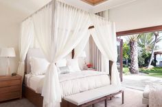 a bedroom with a canopy bed and white drapes on the ceiling, windows to outside