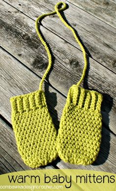 a pair of yellow knitted baby mittens sitting on top of a wooden table