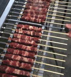 several skewers of meat are being cooked on a bbq with tongs