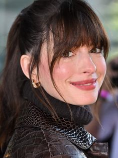 a close up of a person wearing a leather jacket and smiling at the camera with her hair pulled back