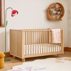 a wooden crib in a child's room with pink and yellow accessories on the wall