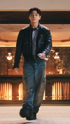 a man in jeans and a leather jacket is holding a remote control while standing on the floor