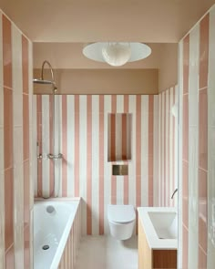 a bathroom with pink and white stripes on the walls, tub, toilet and sink