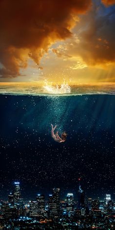 a person floating in the ocean with city lights behind them and an orange sky above