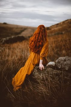 a woman with red hair is sitting on a rock in the middle of a field