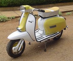 a yellow and white scooter is parked on the side of the road in front of some bushes