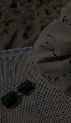 a pair of sunglasses sitting on top of a mat next to a bag and sand