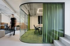 an office with green curtains on the wall, and a person walking down the stairs