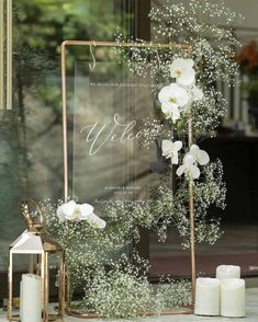 white flowers and baby's breath are displayed in front of a glass sign that says welcome