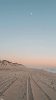 a sandy beach with tracks in the sand and a half - moon rising above it