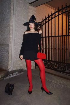 a woman in black dress and red tights standing next to a cat