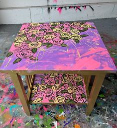 a table painted with pink, yellow and purple flowers on it in front of a wall