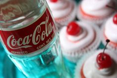 a bottle of coca cola sitting next to cupcakes