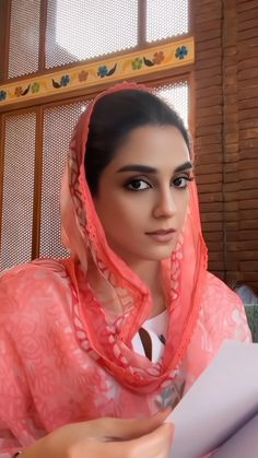 a woman in an orange shawl is looking at something on her hand and holding a piece of paper