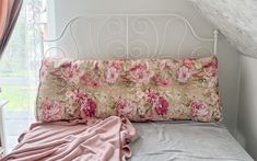 a bed with pink flowers on it in a room next to a window and a white iron headboard