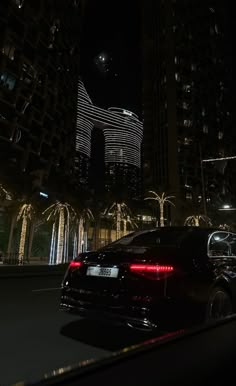 a car is driving down the street at night in front of tall buildings and palm trees