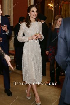 a woman in a white dress standing next to other people at a formal event and holding a wine glass