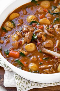 a white bowl filled with stew and potatoes on top of a wooden table next to a napkin