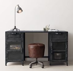 an office desk with a leather stool and lamp on the top, in front of a white wall