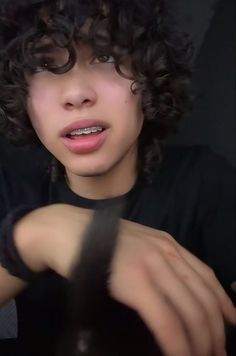 a close up of a person with curly hair wearing a black shirt and bracelets