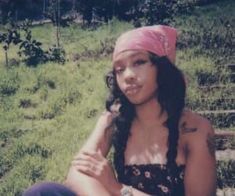 a woman sitting in the grass wearing a pink bandana and looking at the camera