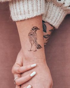 a woman's arm with a bird and flower tattoo on it, sitting next to her hand