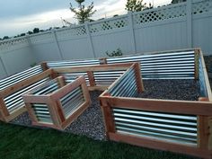 several wooden raised garden beds sitting on top of some gravel in the grass near a fence