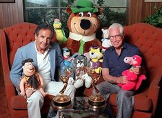 two men are sitting on a couch with stuffed animals in front of them and one man is holding a teddy bear