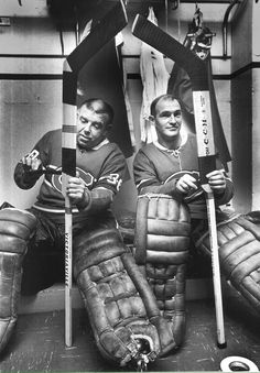 black and white photograph of two men holding baseball bats in the dugout with catchers mitts