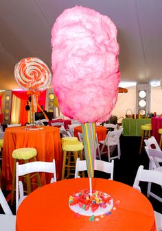 an orange table topped with a giant pink lollipop next to white chairs and tables