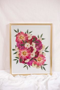 pink and white flowers are displayed in a gold frame on a white bedding sheet