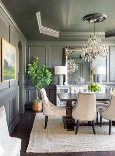 an elegant dining room with gray walls and white chairs, chandelier above the table