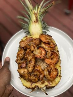 a pineapple and shrimp dish on a white plate with a hand holding it up