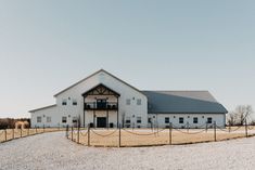 a large white barn sitting on top of a dry grass field next to a fence