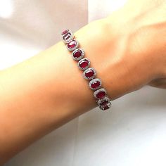 This breathtaking genuine ruby and white topaz bracelet makes a gorgeous gift or a decadent treat just for you. The blazing red of the ruby creates a striking contrast to the sparkling white topaz stones surrounding them. Set in 925 sterling silver with an anti tarnish platinum finish, it looks sparkling and luxurious on your wrist. Measures 6''  in length with a 2.5''  silver extension and approximately 7 mm by 9 mm oval stone with white topaz surround. The bracelet is made up of 23 ruby and topaz stones. July birthstone. 40th Wedding Anniversary. Rubies often contain inclusions. These flaws are not looked upon as negative attributes for rubies.  Indeed, these inclusions are considered part of the character of the stone and are there to assure the purchaser of a natural stone. With your f Red Oval Diamond Bracelet As Gift, Red Oval Diamond Bracelet For Gift, Red Oval Diamond Bracelet Gift, Red Round Bracelets With Diamond Accents, Red Bracelets With Diamond Accents, Red Diamond Bracelet With Gemstone, Fine Jewelry Red Cubic Zirconia Tennis Bracelet, Red Diamond Oval Bracelet, Red Oval Diamond Bracelet