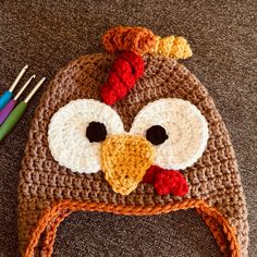 a crocheted hat with a turkey on it and two knitting needles next to it