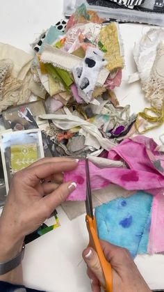 a person cutting fabric with scissors on top of a white table covered in scraps