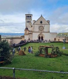 people are standing in front of an old church with many trees and bushes around it